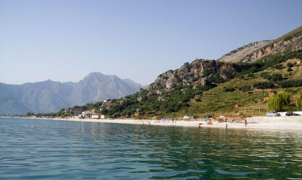 Badegäste am langen Strand von Borsh mit den Bergen der albanischen Riviera im Hintergrund.